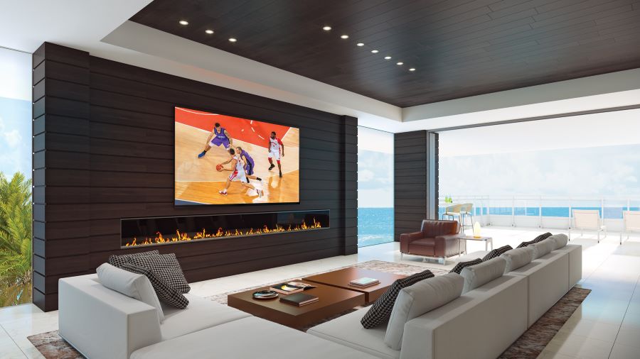 A living area overlooking the ocean with a large flat-screen TV above a lit fire feature.